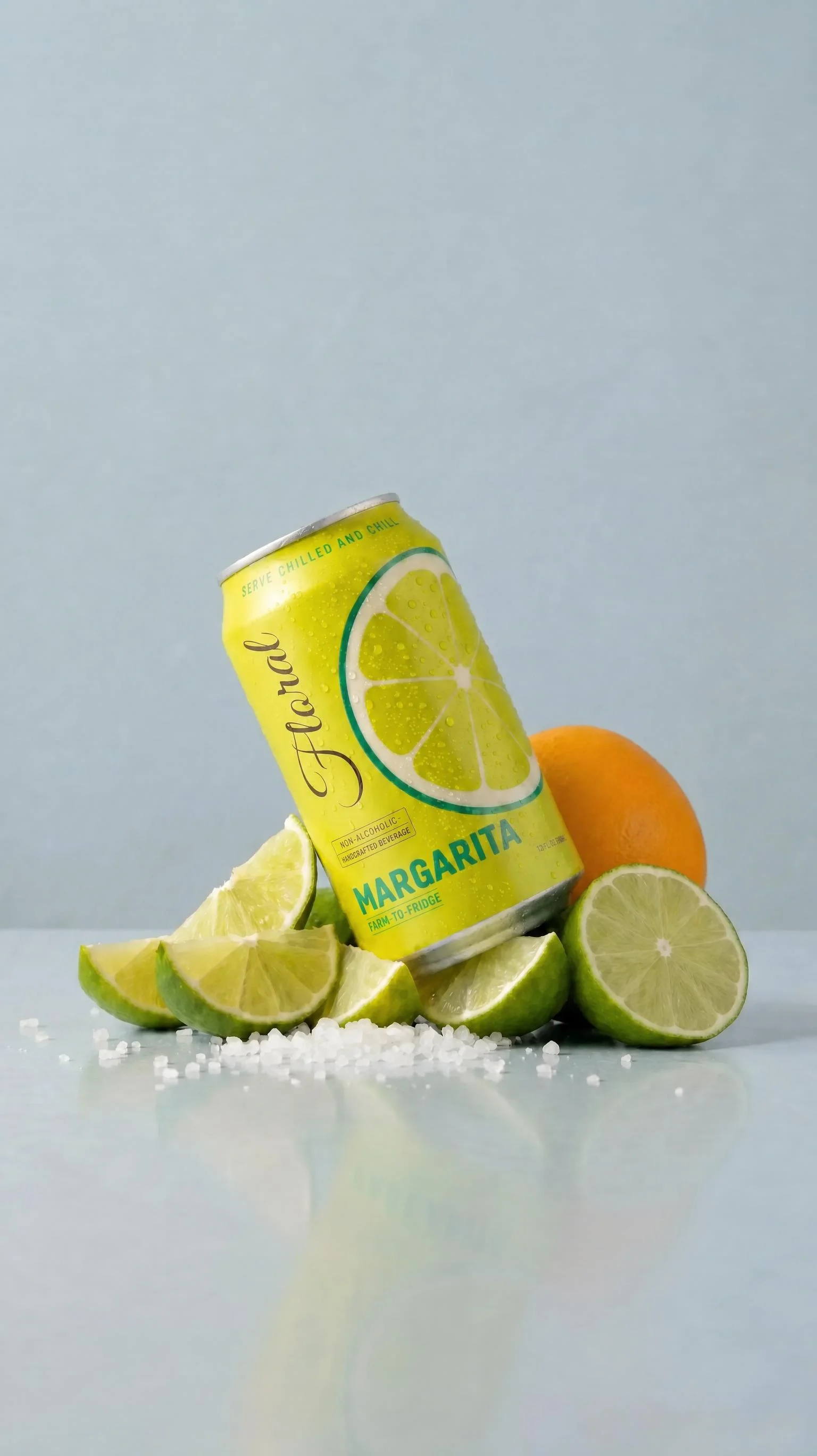 A chilled Floral Margarita can resting on cut limes, salt and citrus against a soft studio backdrop